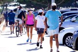 People wearing masks with shorts and t-shirts with a row of cars in the background.