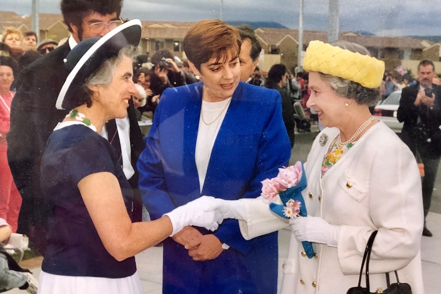 Woman wearing navy hat shakes hands with Queen Elizabeth II. 