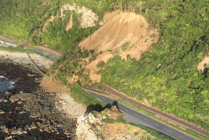 Mound of of dirt and debris blocks a highway and destroys train tracks right next to the sea.