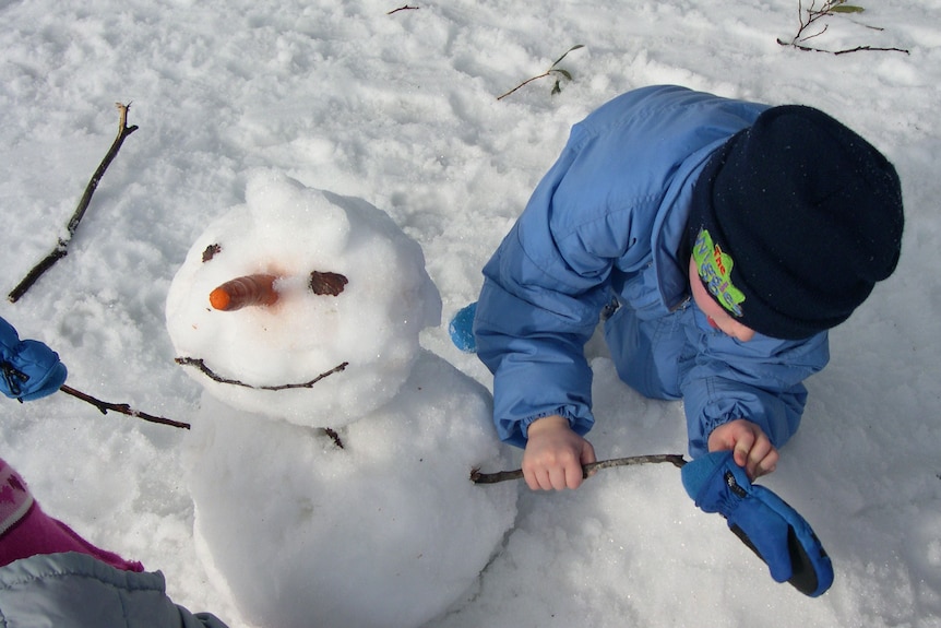 Enfants construisant un bonhomme de neige avec carotte pour nez aux champs de neige du mont Selwyn, NSW.