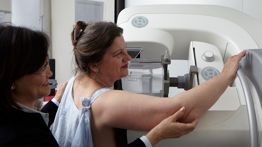 A woman having a mammogram with an assistant behind her