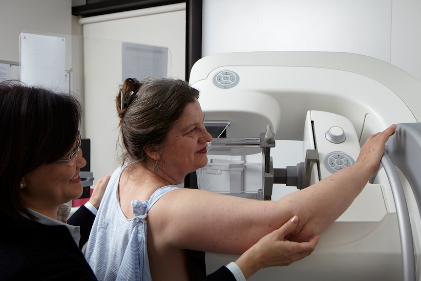 A woman having a mammogram with an assistant behind her