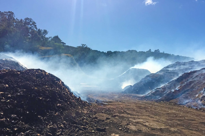 Multiple large piles of waste smoulders with smoke at a tip.
