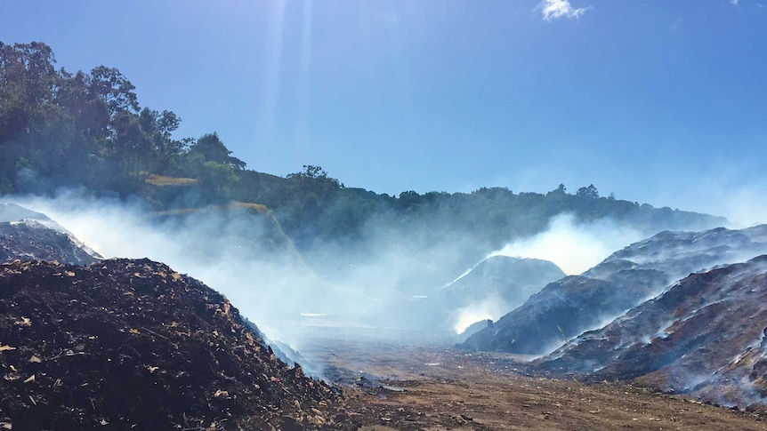 Multiple large piles of waste smoulders with smoke at a tip.