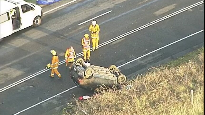 A vehicle rolled on its roof on a road with SES officers nearby