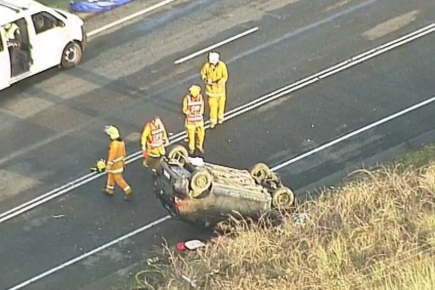 A vehicle rolled on its roof on a road with SES officers nearby