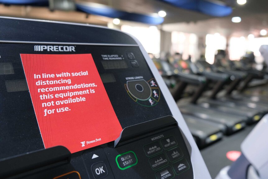 A social distancing sign on a treadmill in a gym.