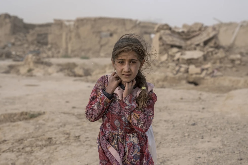 A young girl standing in front of destroyed buildings in the sand