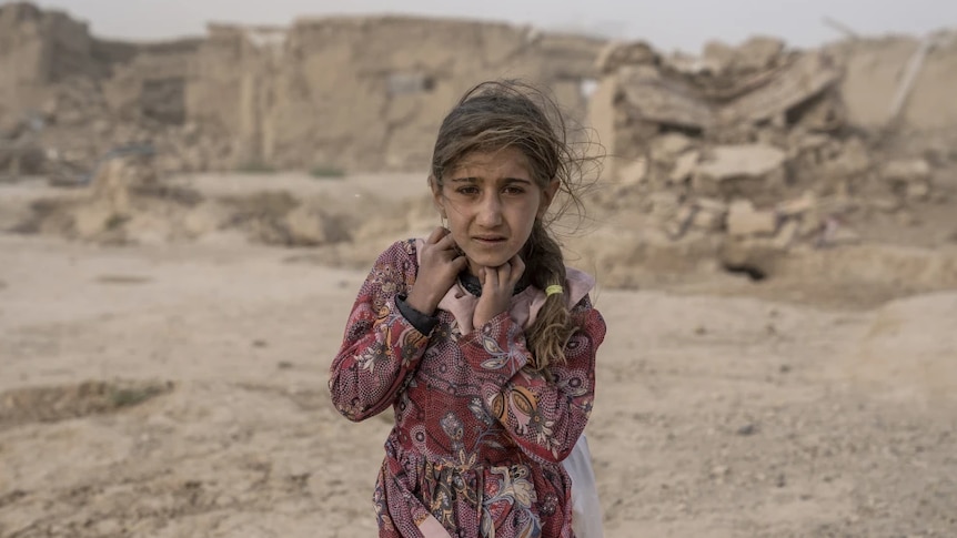 A young girl standing in front of destroyed buildings in the sand