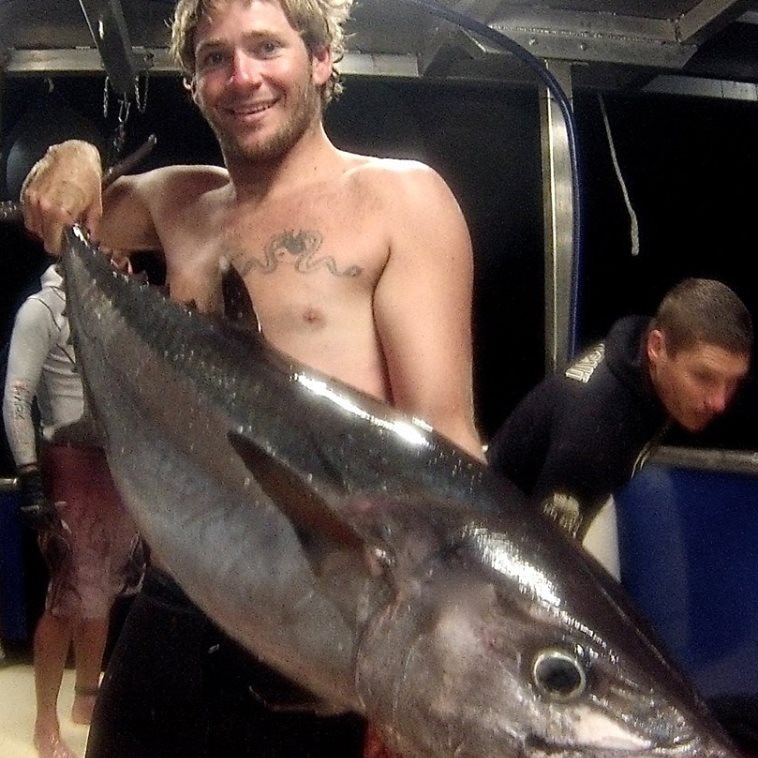 Zac Feeney standing on a boat deck holding a large fish.