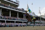 A jockey raises his fist in victory, riding a horse in the Kentucky Derby, in front of a massive grandstand of fans.