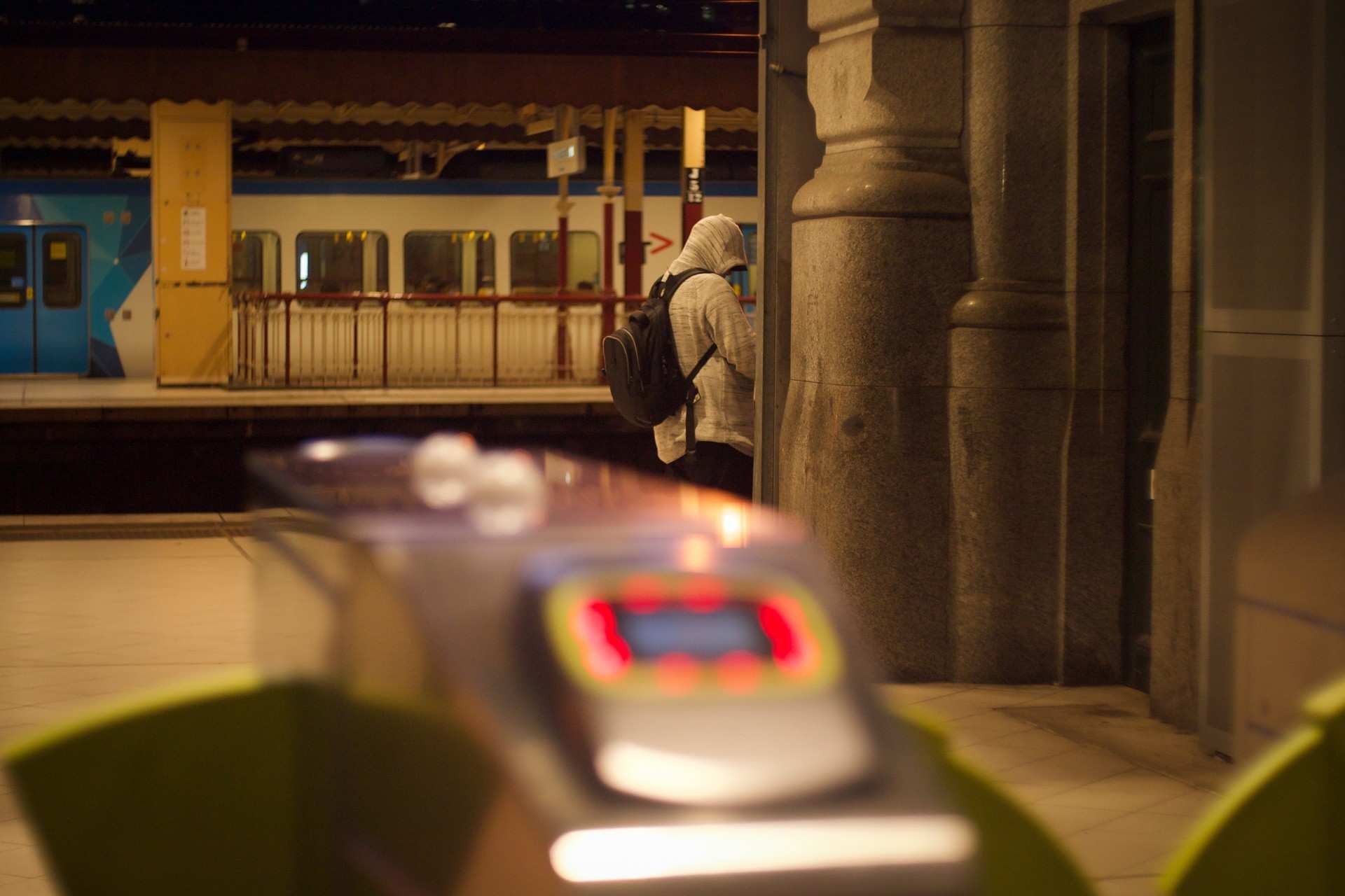 Behind the ticket barriers at Flinders Street Station, a man in a hoodie waits for a train on the platform.