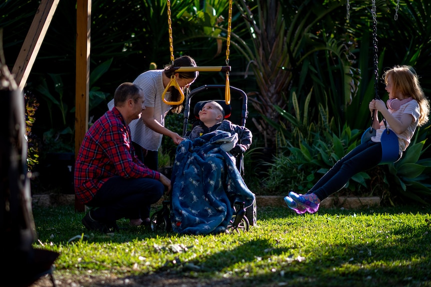 A mother and father with a child in a wheelchair, and another child on a swing.