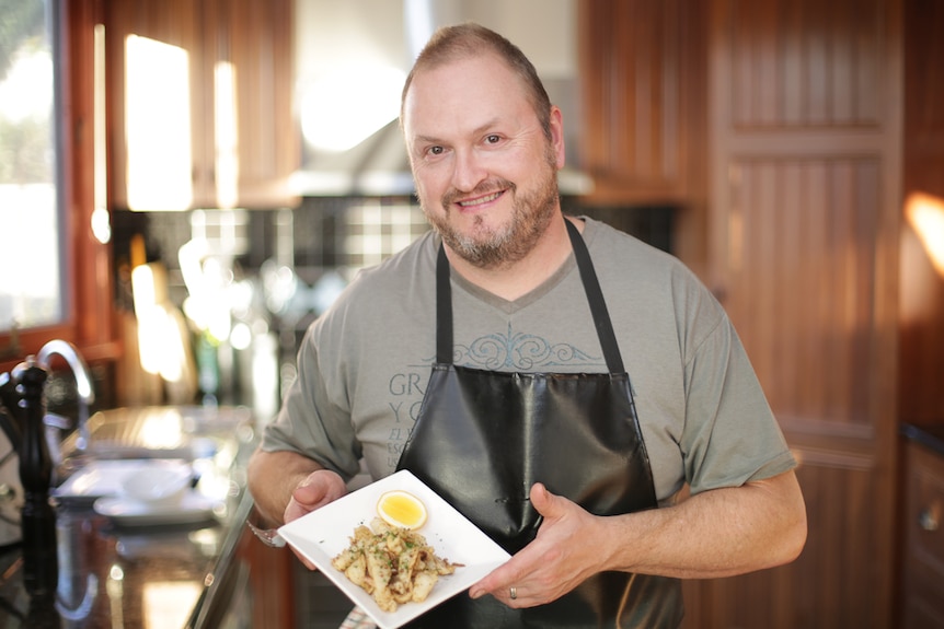 Chef James Maffescioni standing in a kitchen holding a plate of cooked squid to depict how to prepare and cook squid.