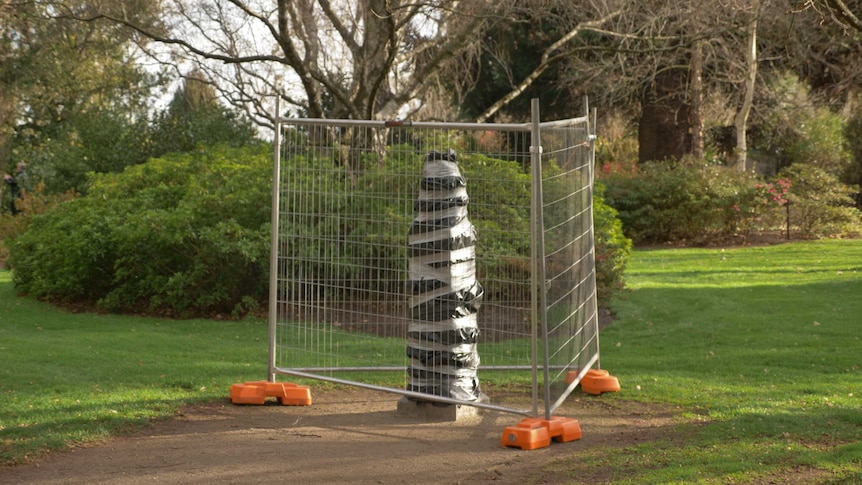 A bronze bust in the Ballarat Botanical Gardens wrapped up in black plastic with grey tape around it, fenced off.