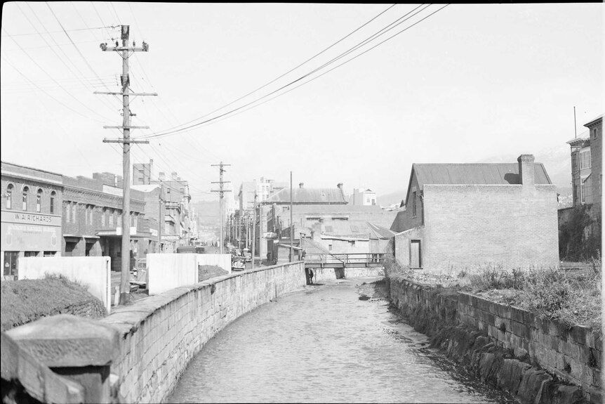 Black and white image of a small river, powerlines and brick buildings