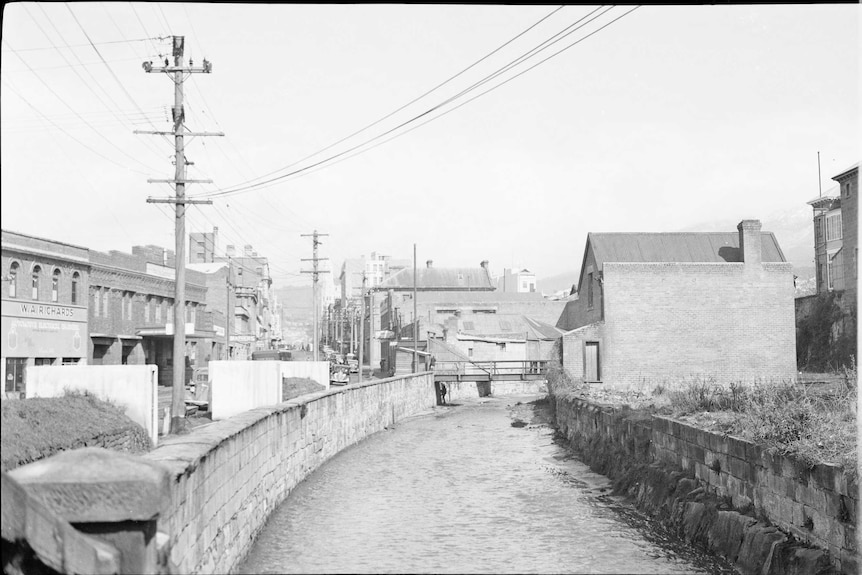 Black and white image of a small river, powerlines and brick buildings