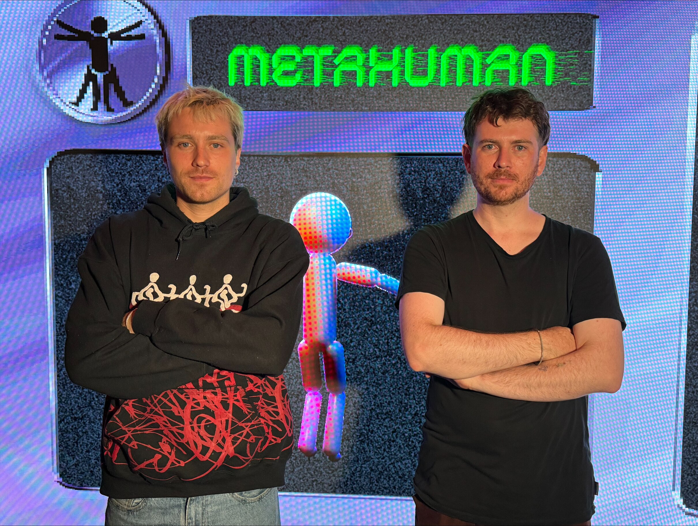 Two men standing with their arms crossed in front of a digital screen that says metahuman