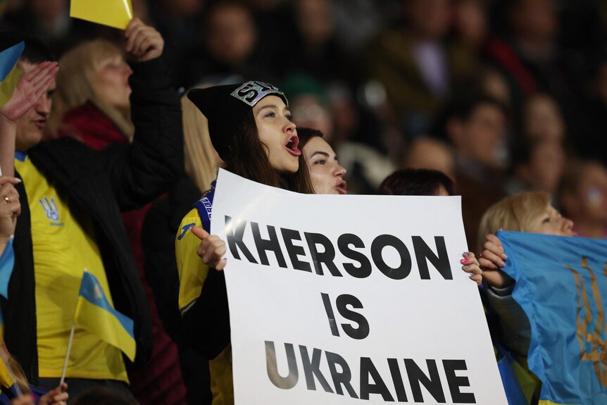 A Dynamo Kyiv fan displays a banner reading 'Kherson is Ukraine'.