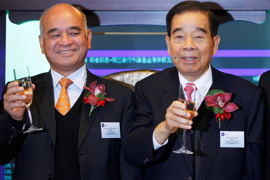 Two Chinese men wearing suits and holding champagne glasses.