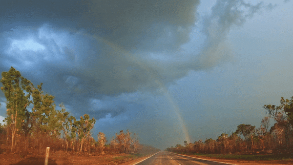 A GIF of a lightning bolt striking the ground near an outback road with a rainbow in the background.