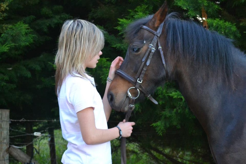 A young girl stands next to a horse. 