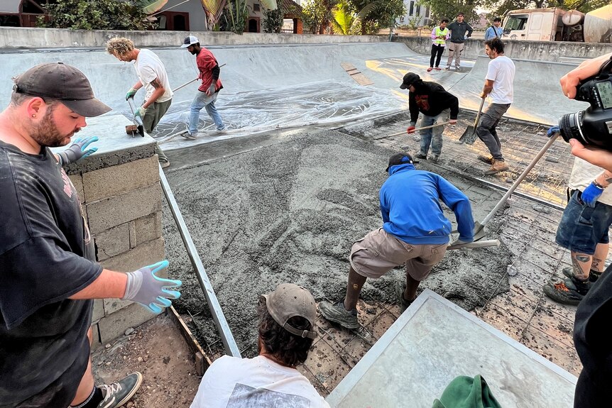 A group of people of various ethnicities and clothing working on a cement structure in a community.