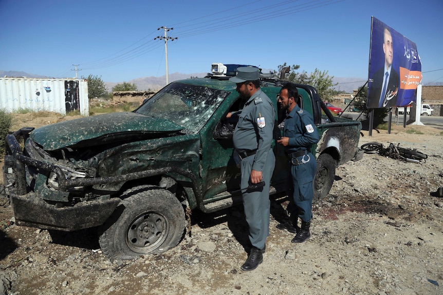 Afghan police inspect the site of a suicide attack, including a large ute that has been destroyed by the blast.