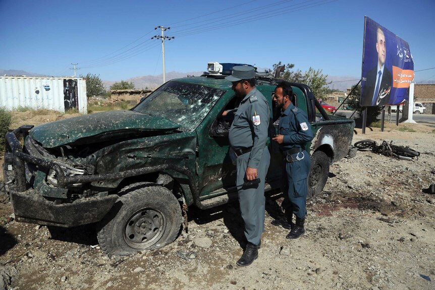 Afghan police inspect the site of a suicide attack, including a large ute that has been destroyed by the blast.