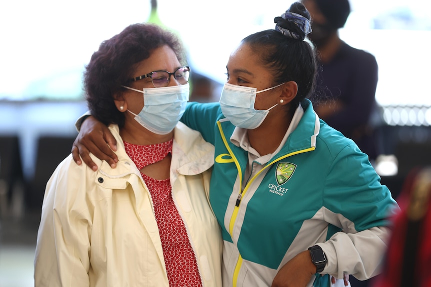 Alana King puts her arm around her mother, the pair wear masks as they greet each other at the airport