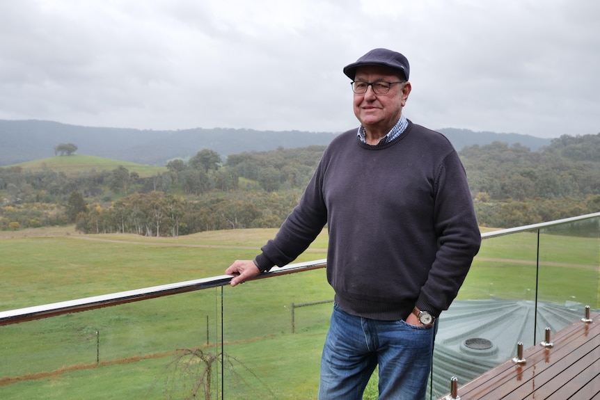 An older man standing on a balcony overlooking a paddock