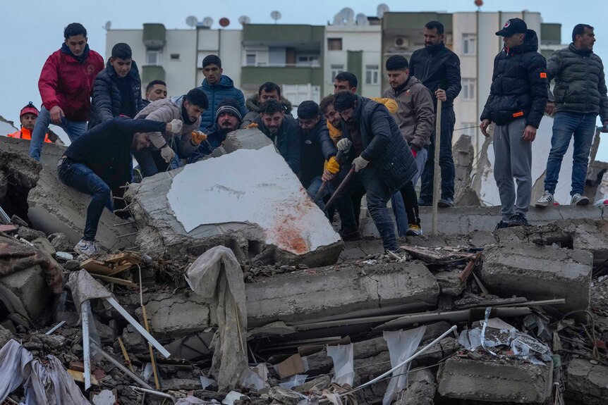Men stand on one side of the rubble as they work to lift pieces free. 