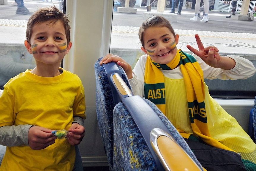 two siblings, a boy and a girl, sit on the light rail both looking at the camera with the girl holding her hand in peace sign