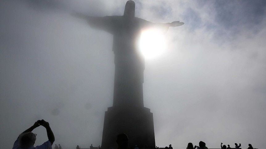 People gather beneath the Christ the Redeemer statue as mist passes over the summit of Corcovado.