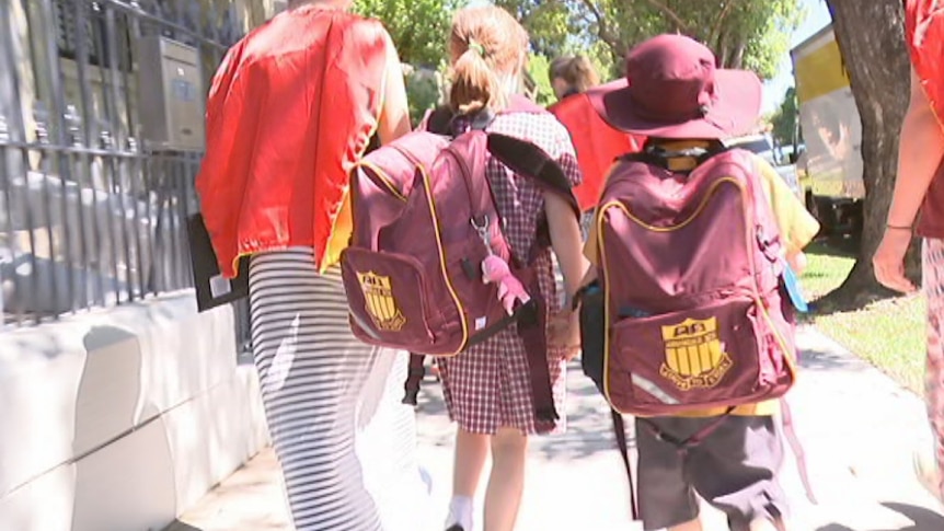 Two students walk with their parents outside a school gate.