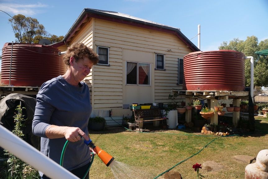 A woman watering with rainwater tanks in the background.