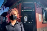 A young woman with long pink hair and a mask stands in from of a door saying Titanic: First class experience