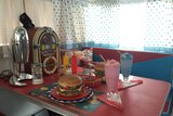 Dukebox, fake hamburger and milkshakes from the 1950s era on an old caravan table.