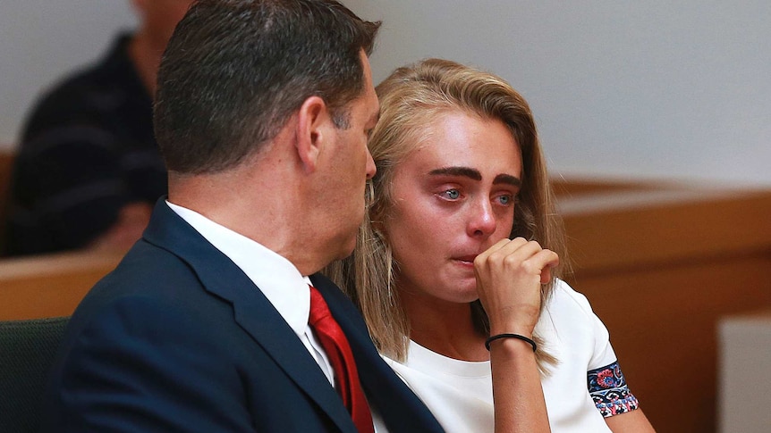 Michelle Carter sits with her lawyer in court. Her face is read and her lips are pursed. Her hand is covering her mouth.