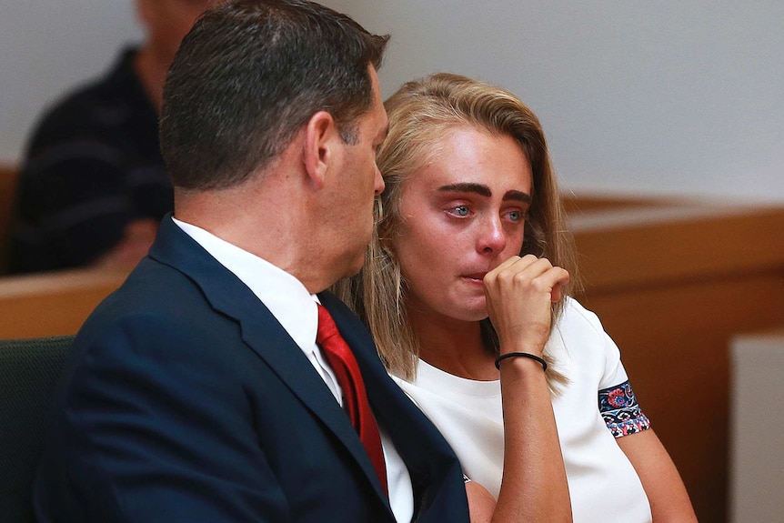 Michelle Carter sits with her lawyer in court. Her face is read and her lips are pursed. Her hand is covering her mouth.