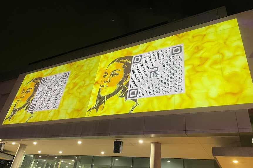 A projected image features a Black woman against a bright yellow screen. A QR code is placed alongside her face.  