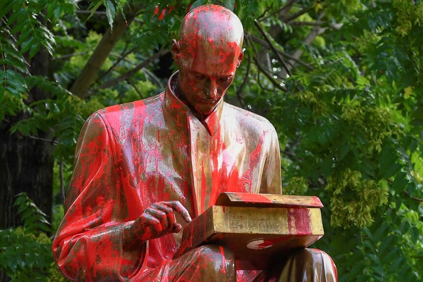 Statue of man at typewriter in park covered in red paint