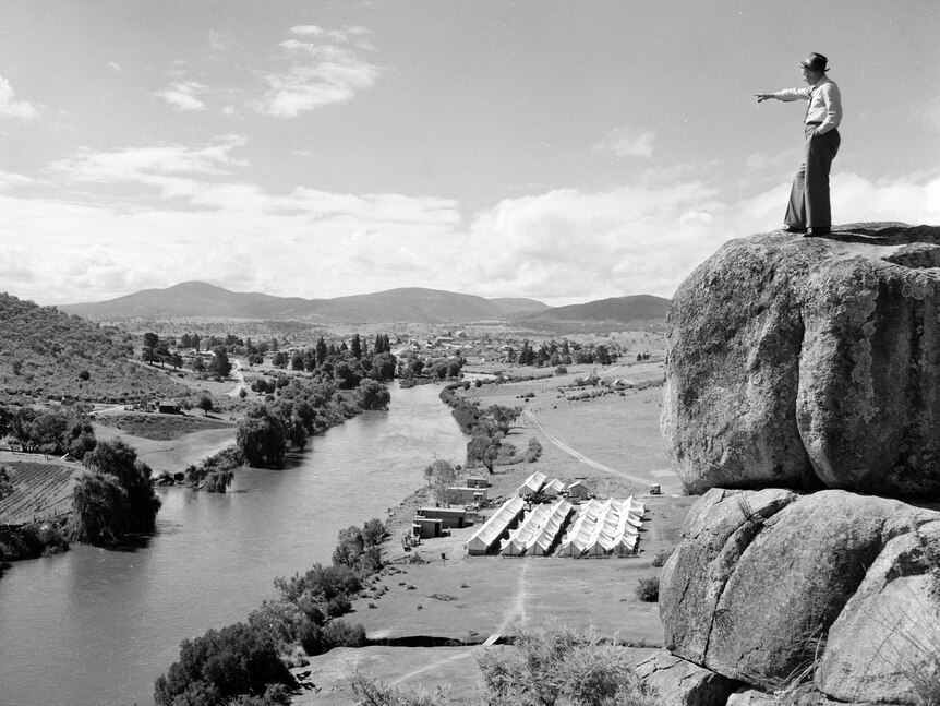 A man stands on a rock ledge that has a view over a valley.