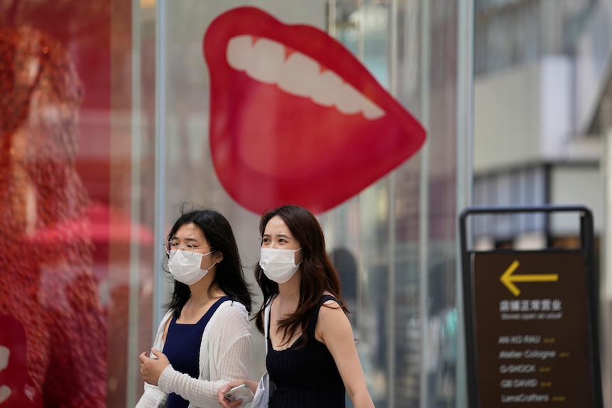 Women wearing masks walks past a store advertisement, Sunday, July 17, 2022, in Beijing.