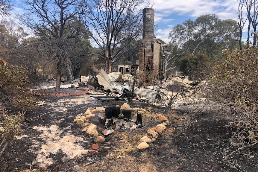 A wide shot of the burnt-out remains of a house destroyed in a bushfire.