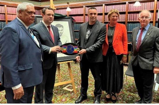 A group of men and women standing in the NSW parliament holding a replica boxing belt.