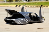 a silver futuristic car with solar panels on it is parked on racetrack with doors open which open upwards. 