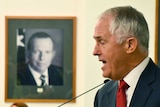 Malcolm Turnbull speaks in front of photo of Tony Abbott