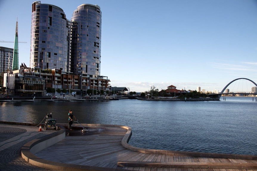 A person operates a pressure cleaner on the boardwalk at Elizabeth Quay