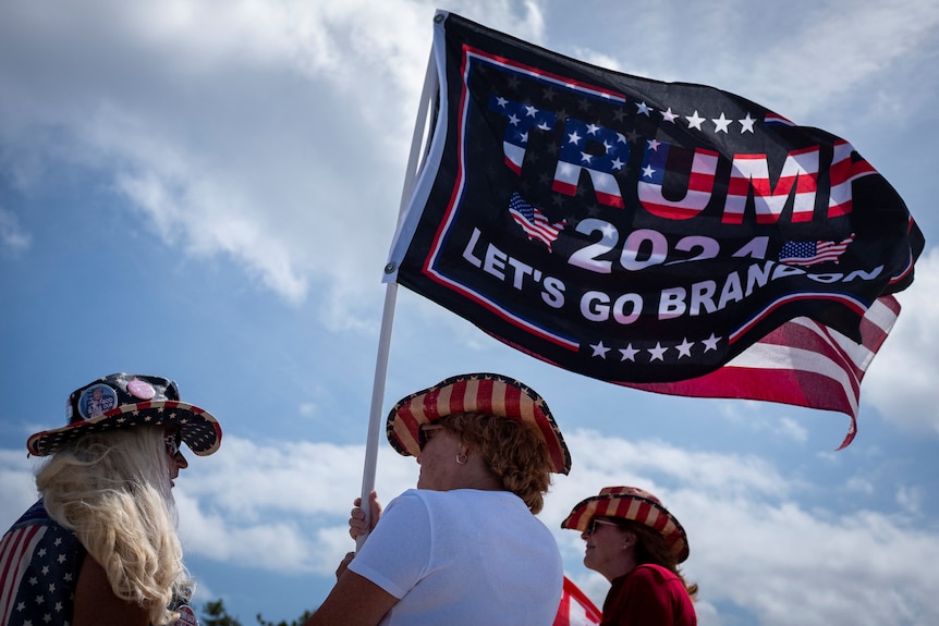A woman  holds a flag which says Trump 2024.
